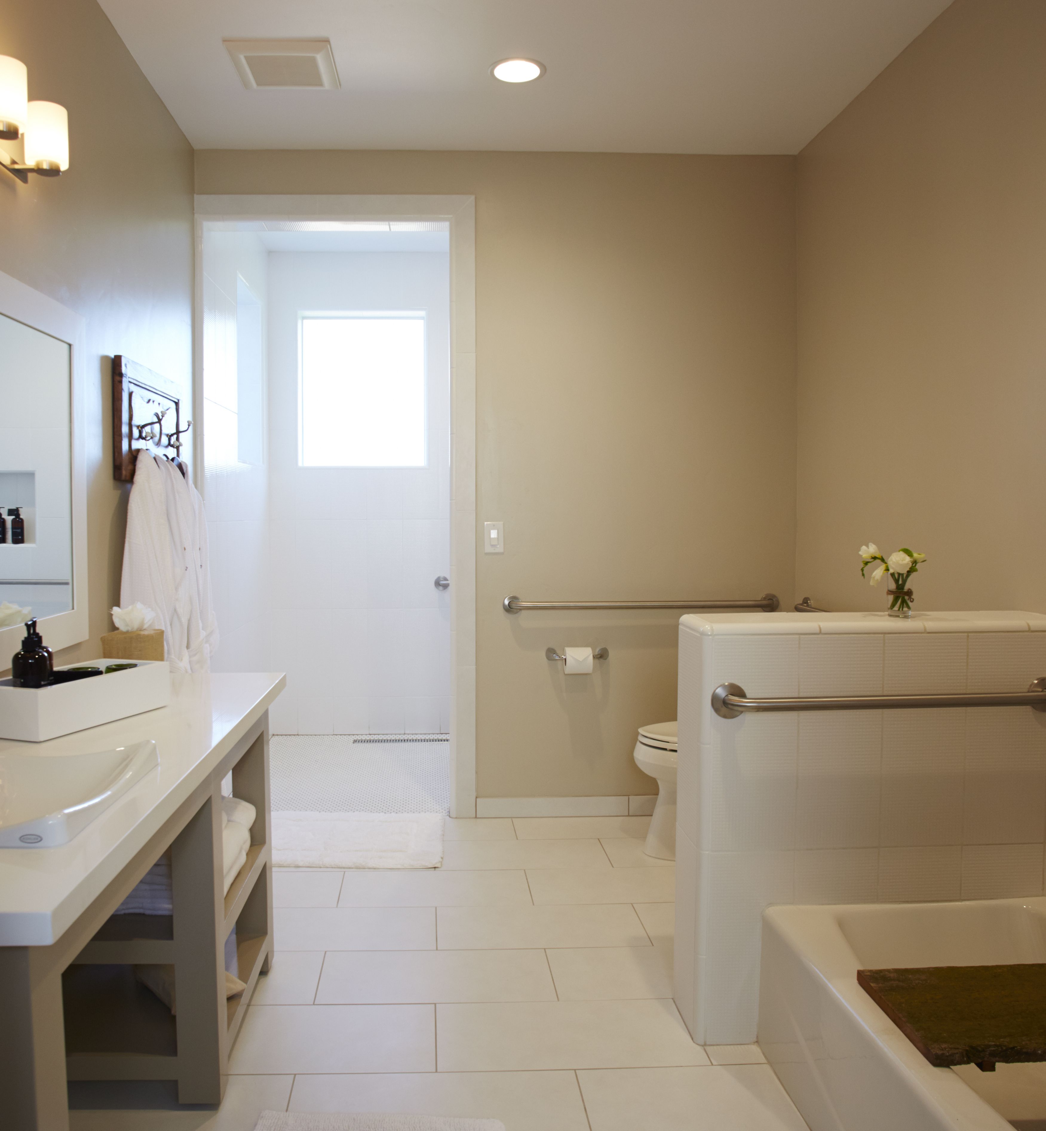 A modern bathroom with a white sink, mirror, and vanity, a shower with a grab bar, and a toilet.