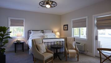 A bedroom with a bed, two chairs, a small table, and a ceiling fan.