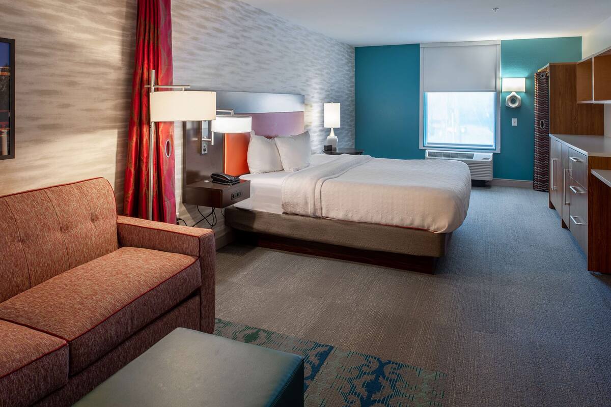 Una habitación de hotel con cama, sofá, escritorio con lámpara, ventana y armario.