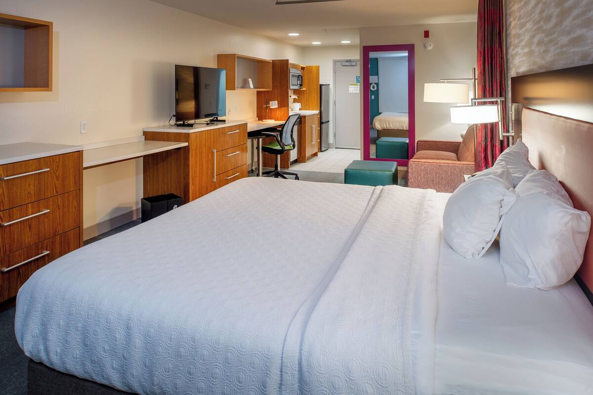 Habitación de hotel con una cama grande, un escritorio con ordenador, televisión y kitchenette.
