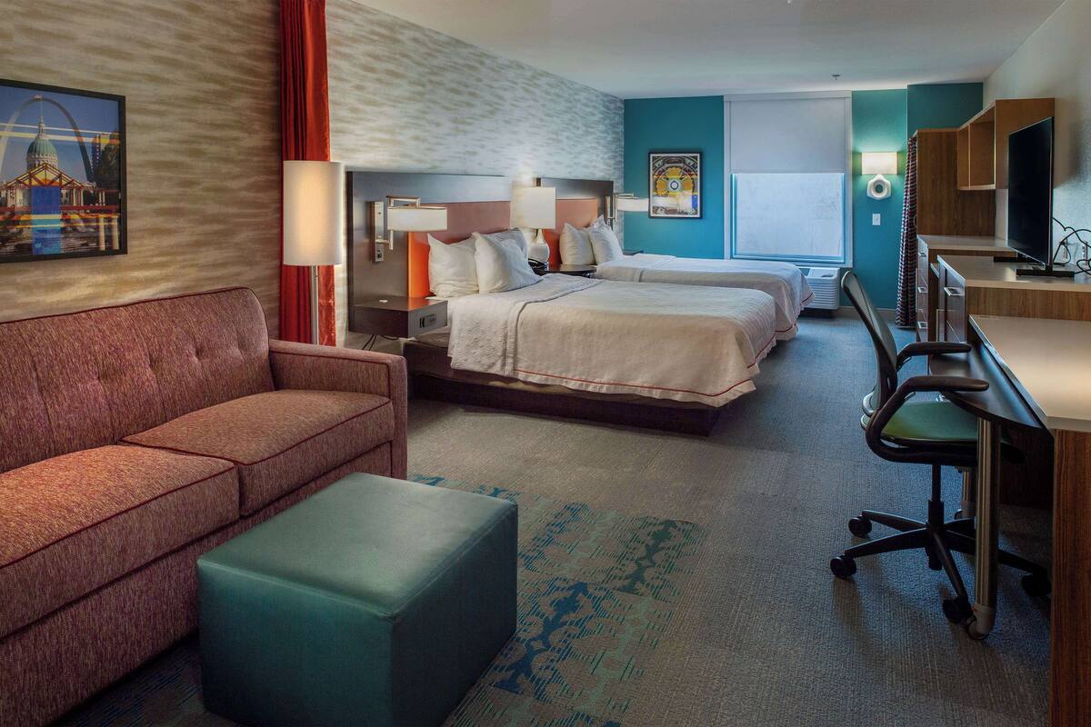 Habitación de hotel con dos camas, un escritorio, una silla, un sofá y una pequeña mesa.