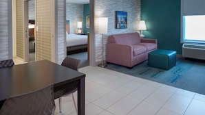 Ein Hotelzimmer mit einem Bett, einem rosa Sofa, einem kleinen Tisch und einem Sessel. Ein Fenster bietet Blick auf ein Gebäude.
