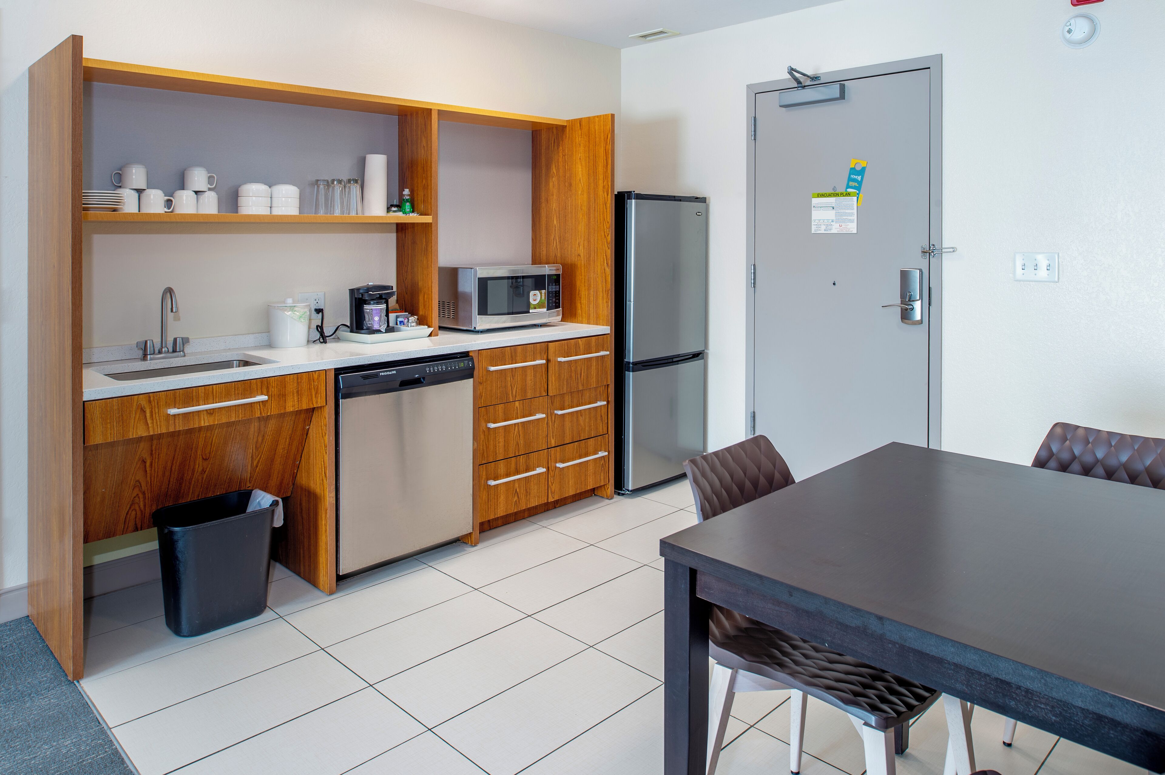 Cocina pequeña y funcional con microondas, refrigerador, lavamanos y armarios de madera.