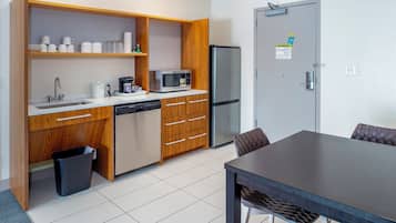 Cocina pequeña y funcional con microondas, refrigerador, lavamanos y armarios de madera.