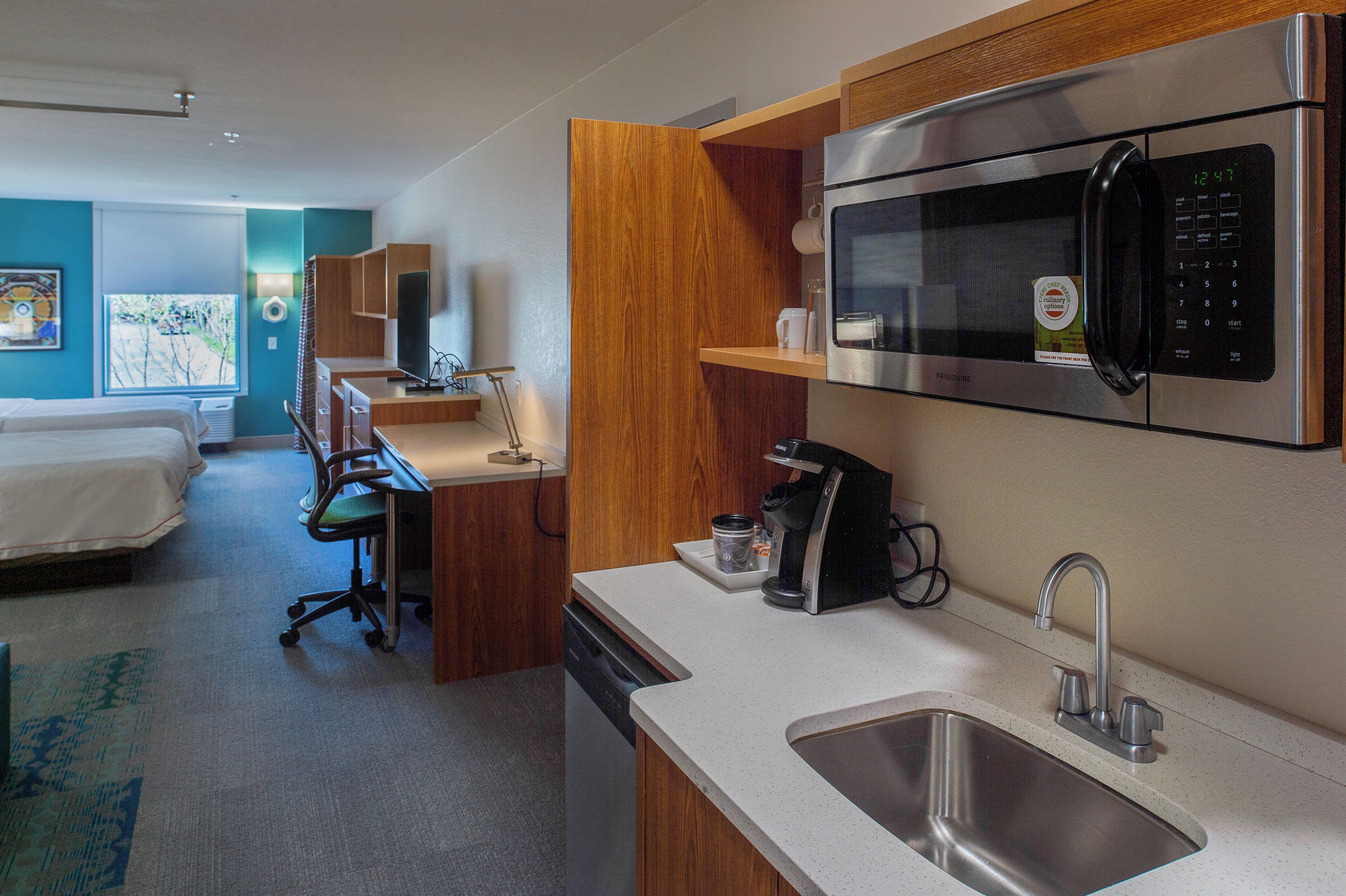 Une chambre d’hôtel compacte comprenant un coin cuisine, un lit, un bureau et une vue sur l’extérieur.