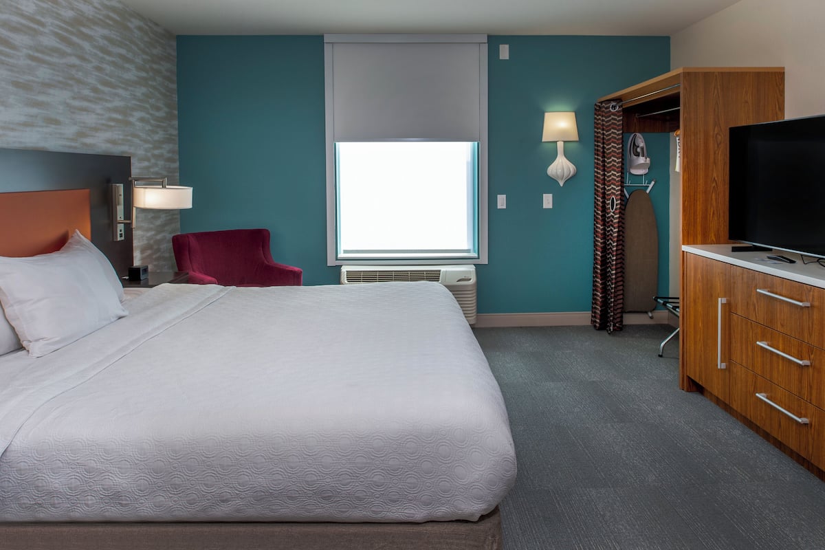Habitación de hotel con una cama grande, un sillón rojo, un televisor y un armario.