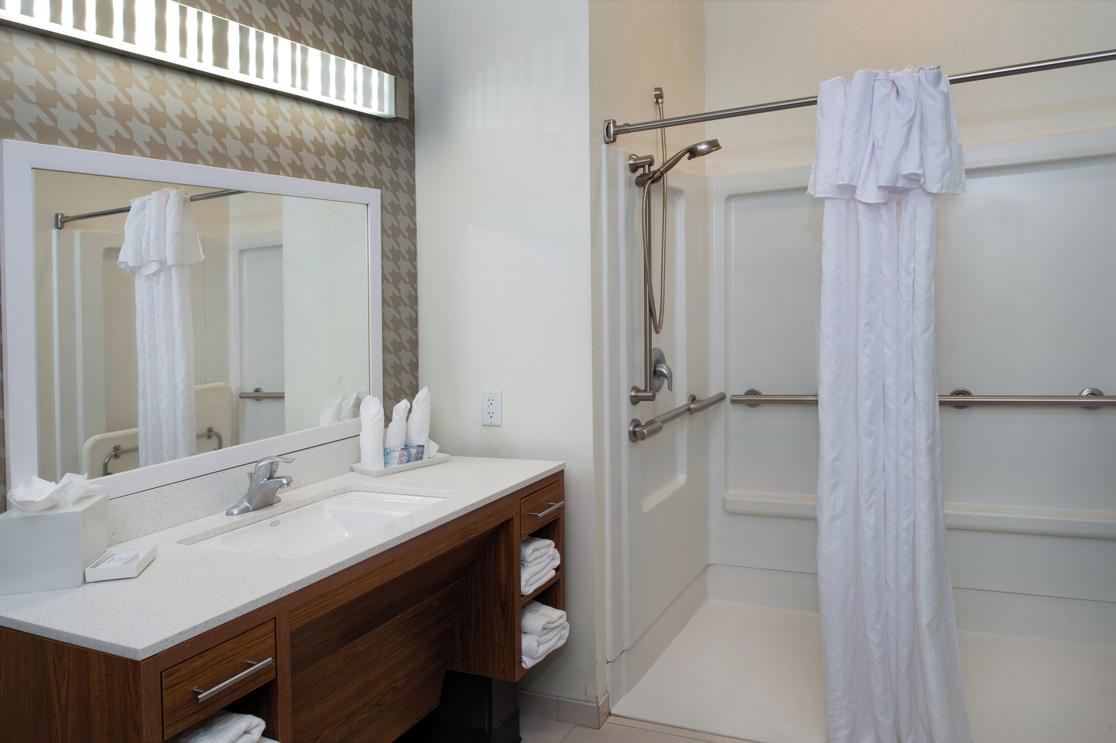 Une salle de bain avec un meuble-lavabo en bois, un grand miroir, une douche avec une porte en verre et un porte-serviettes.
