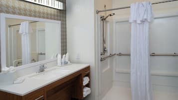 Une salle de bain avec un meuble-lavabo en bois, un grand miroir, une douche avec une porte en verre et un porte-serviettes.