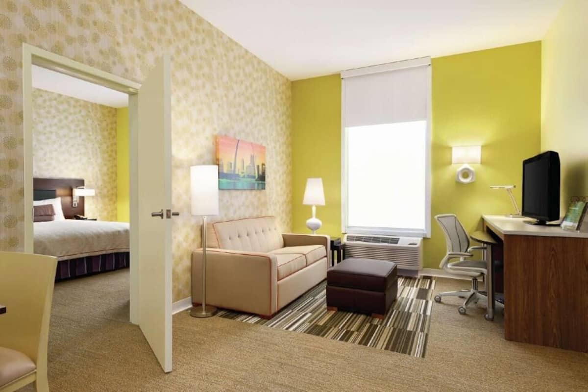 A hotel room with a bed, a sofa, a desk, a chair, a lamp, and a television.