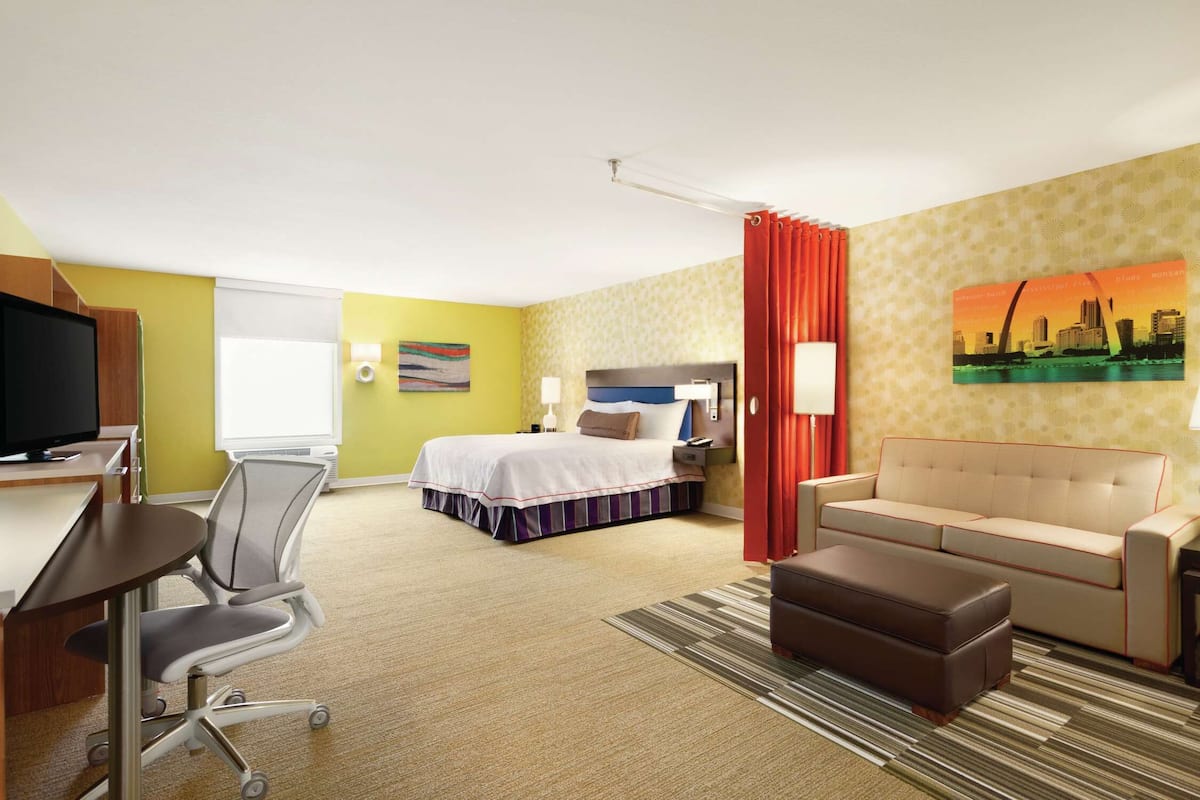 Habitación de hotel con una cama, un escritorio con computadora, una silla, un sofá y un televisor.