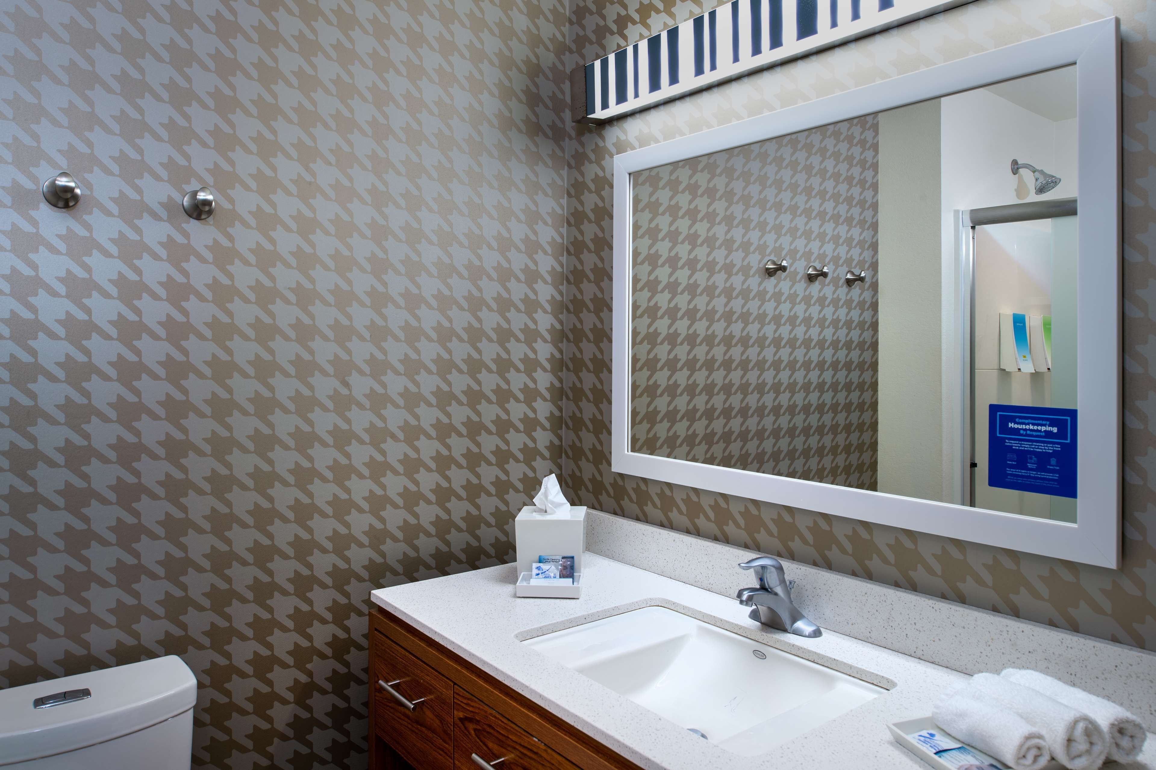 A bathroom with a patterned wallpaper, a white sink, a mirror, and a toilet.