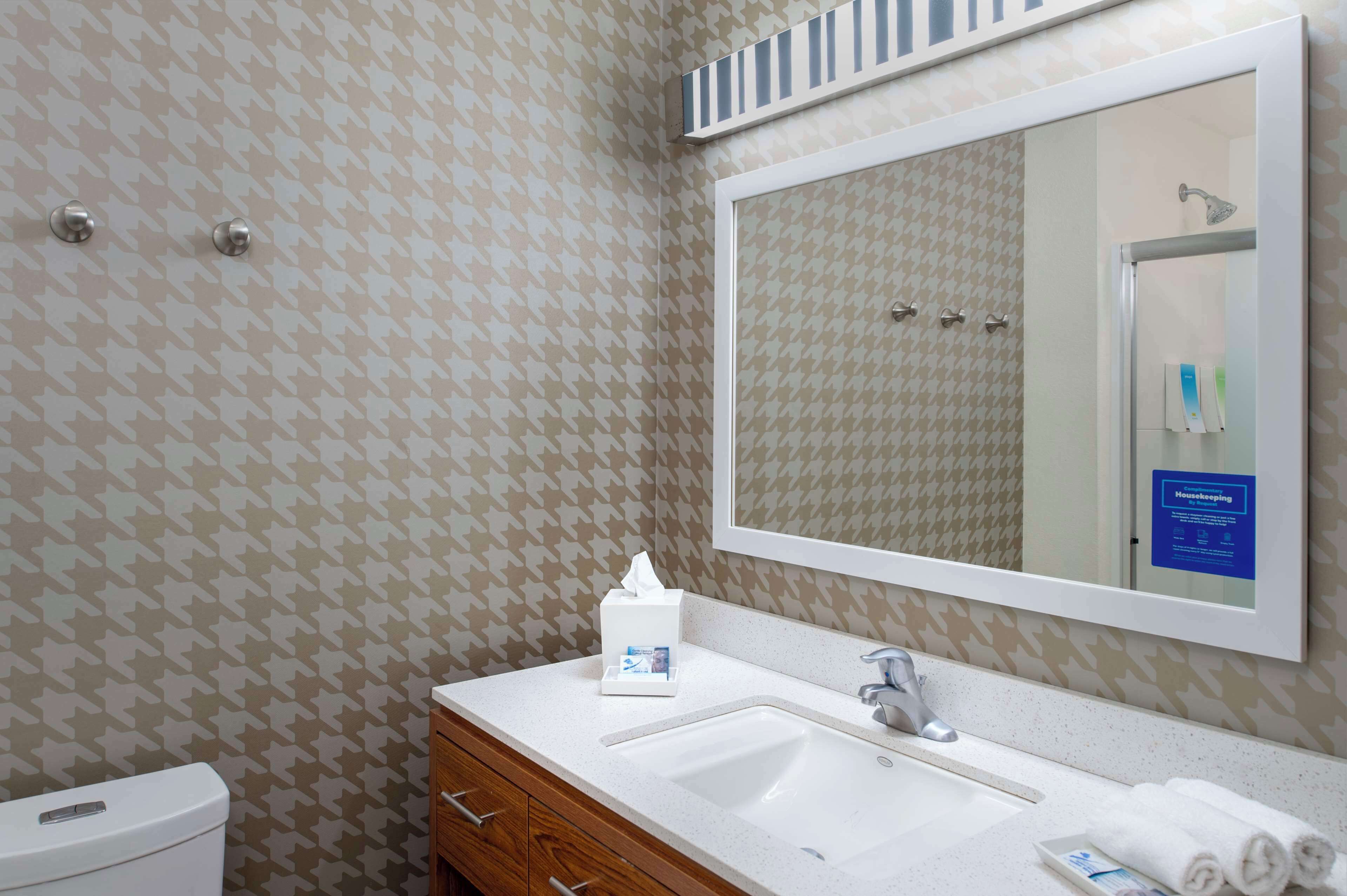 Een badkamer met behang met een patroon, een grote spiegel, een wastafel, een toilet en een handdroger.