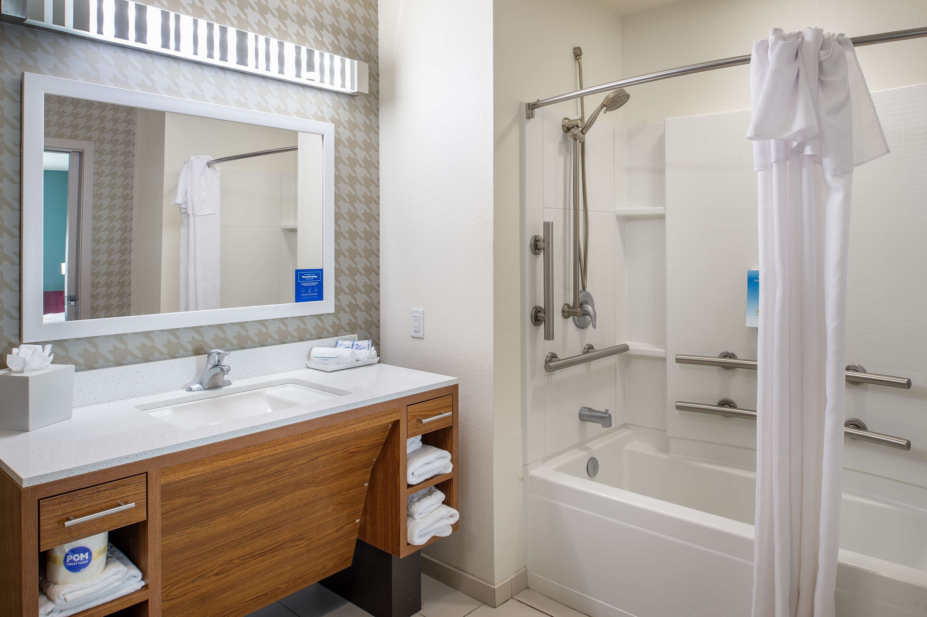 A bathroom with a wooden vanity, a large mirror, a bathtub, and a shower enclosure.