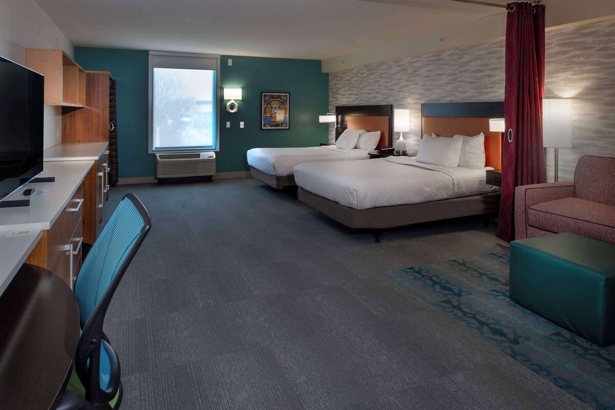 Habitación de hotel con dos camas, un escritorio con computadora, televisión y ventana con vistas.
