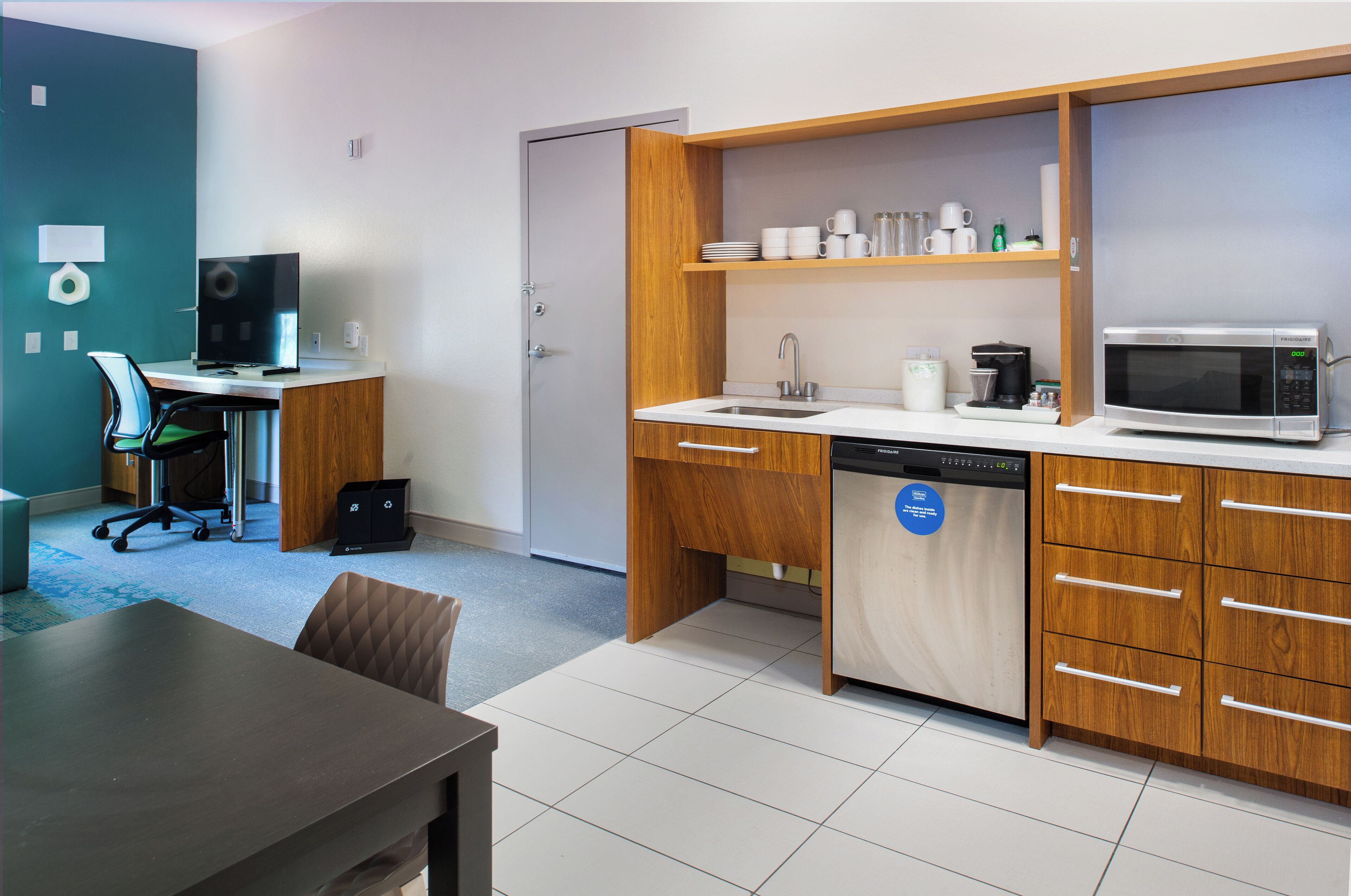 A compact kitchen with a microwave, sink, and wooden cabinets. There's a dining area with a table and chairs.