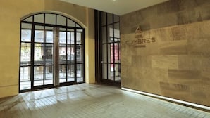 Un vestíbulo de hotel con un amplio puerta de vidrio arqueada, piso de baldosas y pared de piedra con el nombre del hotel.