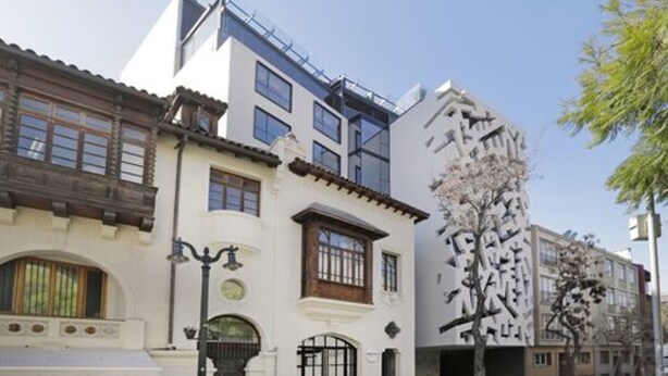 Un edificio con fachada tradicional, sección superior moderna y un árbol en primer plano.