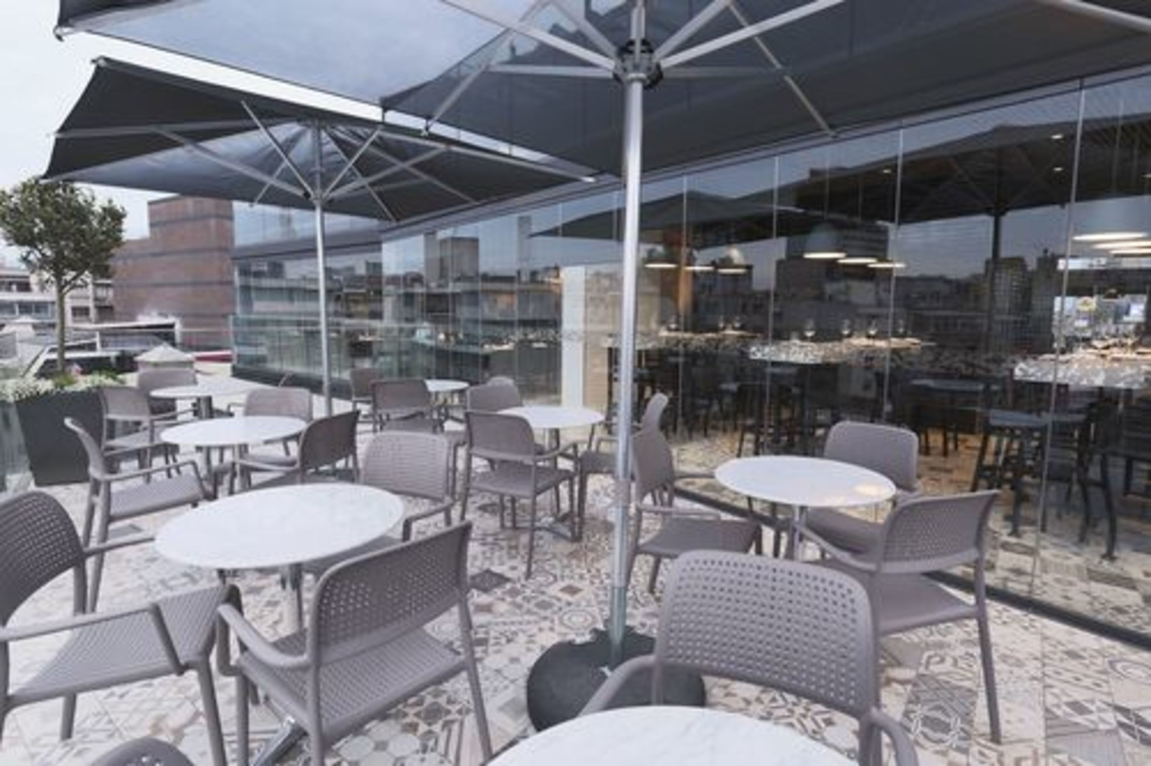 An outdoor seating area with round tables and chairs, covered by a large umbrella.