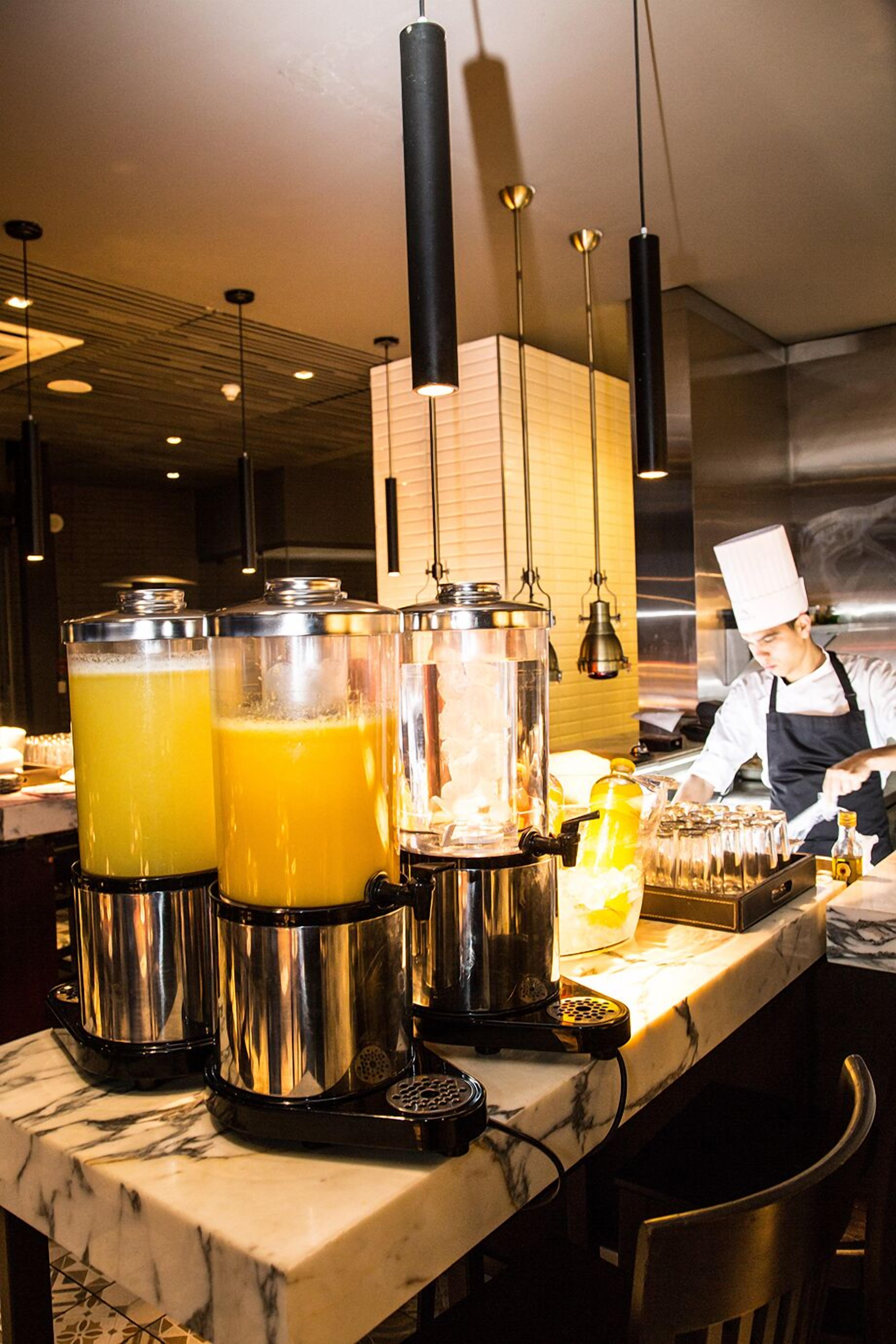 Un espace bar doté d’un comptoir en marbre, de grands distributeurs de jus et d’un chef préparant des boissons.