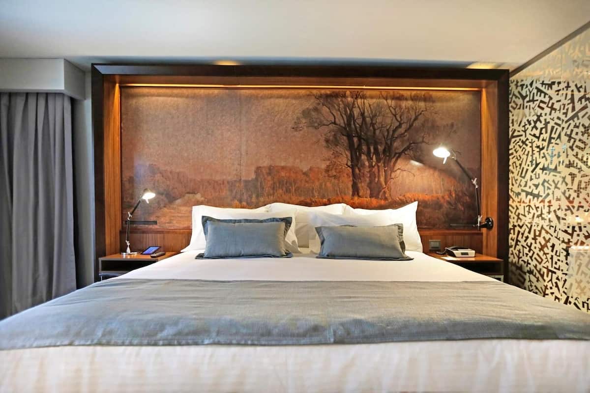 Habitación de hotel con una cama grande, dos mesitas de noche, una lámpara y un mural en la pared.