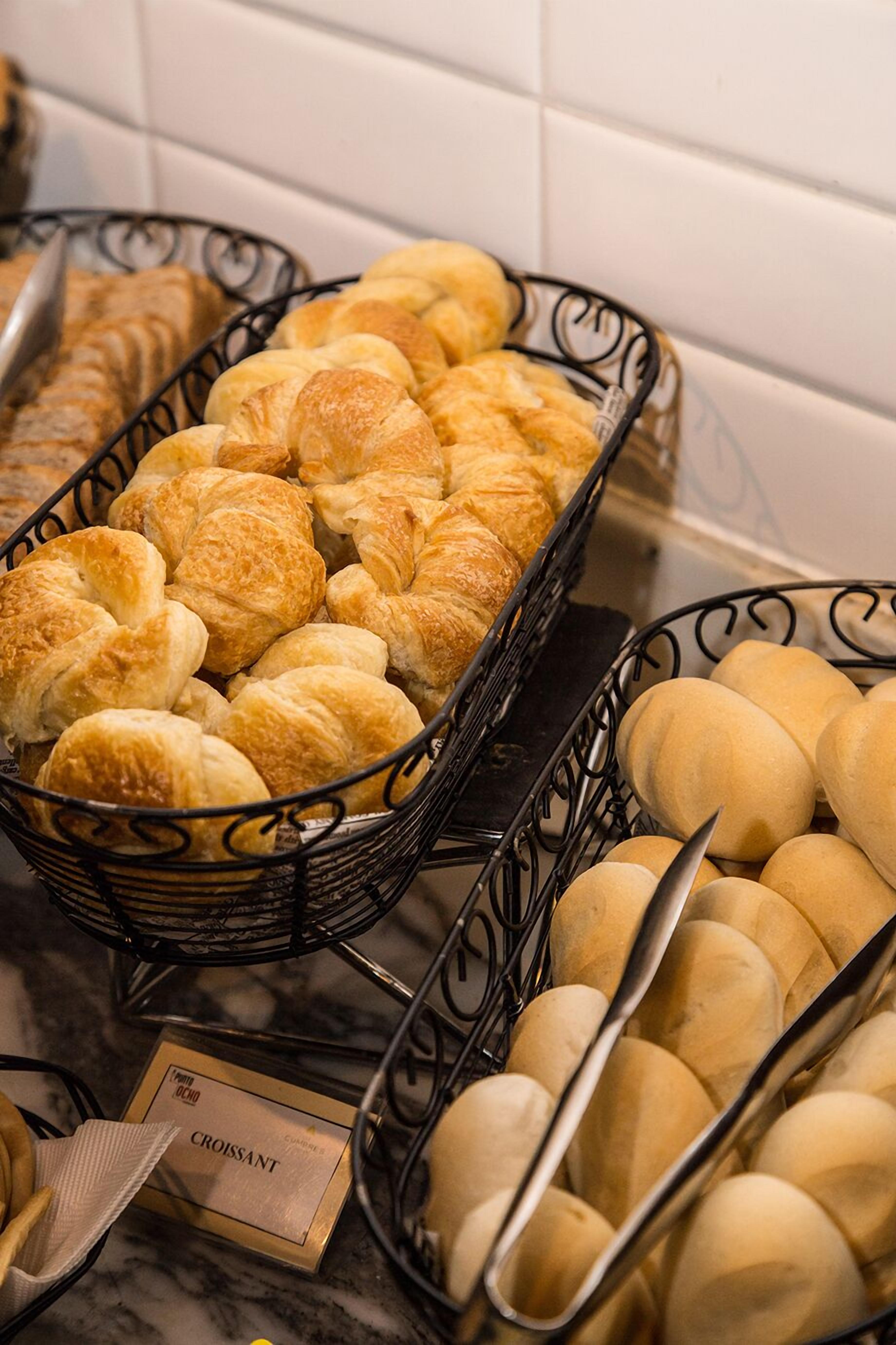A display of assorted pastries in baskets, including croissants and rolls, with a sign indicating 'Croissant' in the foreground.