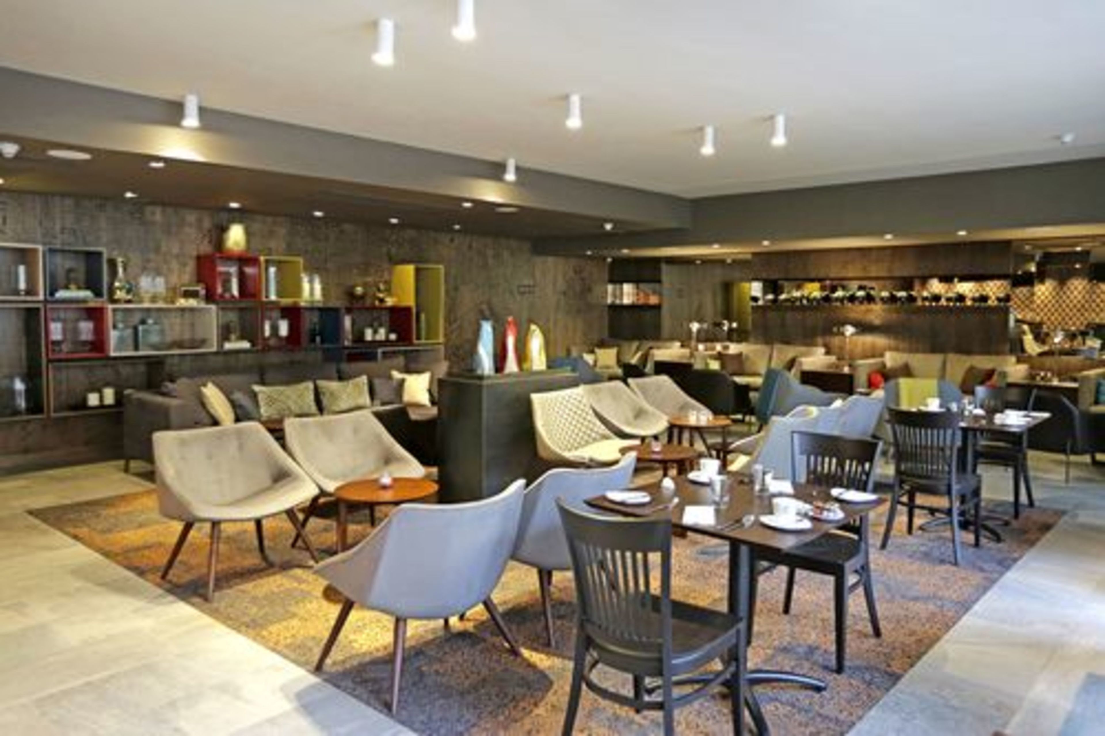 Un moderno espacio de sala de estar con sofás, sillas y mesas, que incluye una barra y estantes con diversos objetos.