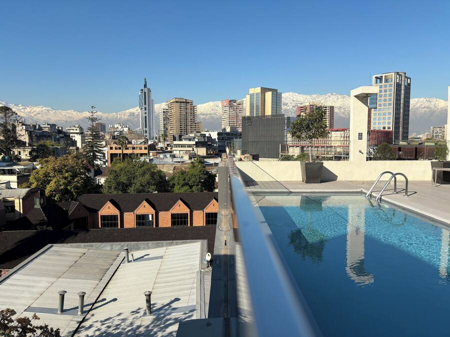 Una piscina en la azotea con vista a un paisaje urbano, que incluye edificios modernos y montañas al fondo.