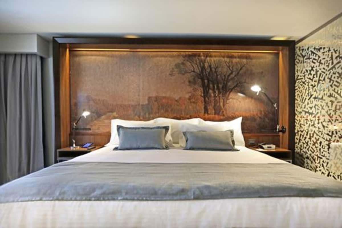 Una cama grande con cabecera, dos mesitas de noche, una lámpara y una pared con diseño decorativo.