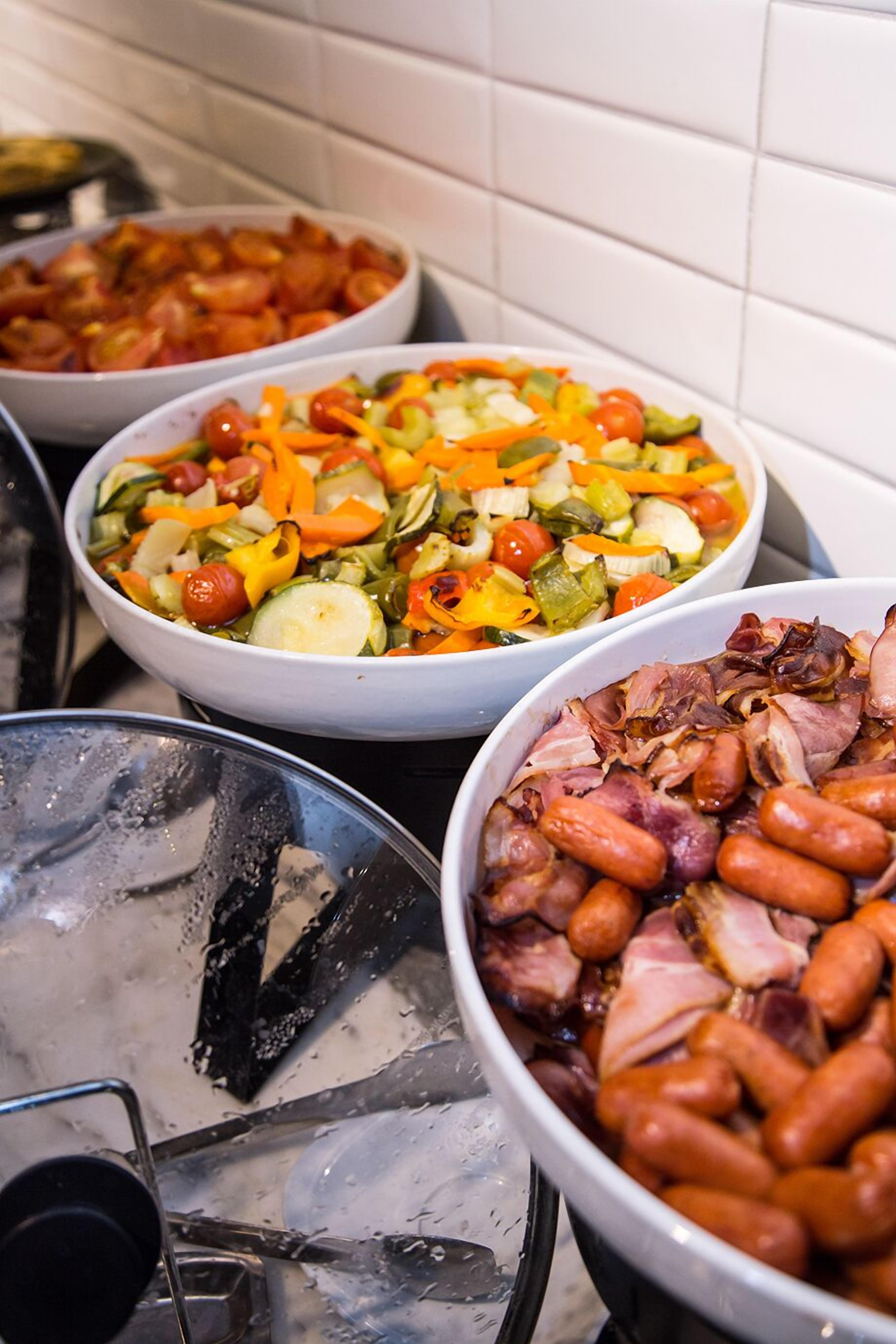 Un bufé con diversos platos, incluyendo ensalada, verduras y salchichas.