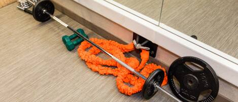 A weightlifting bench with a barbell, green weight plates, and an orange resistance band.