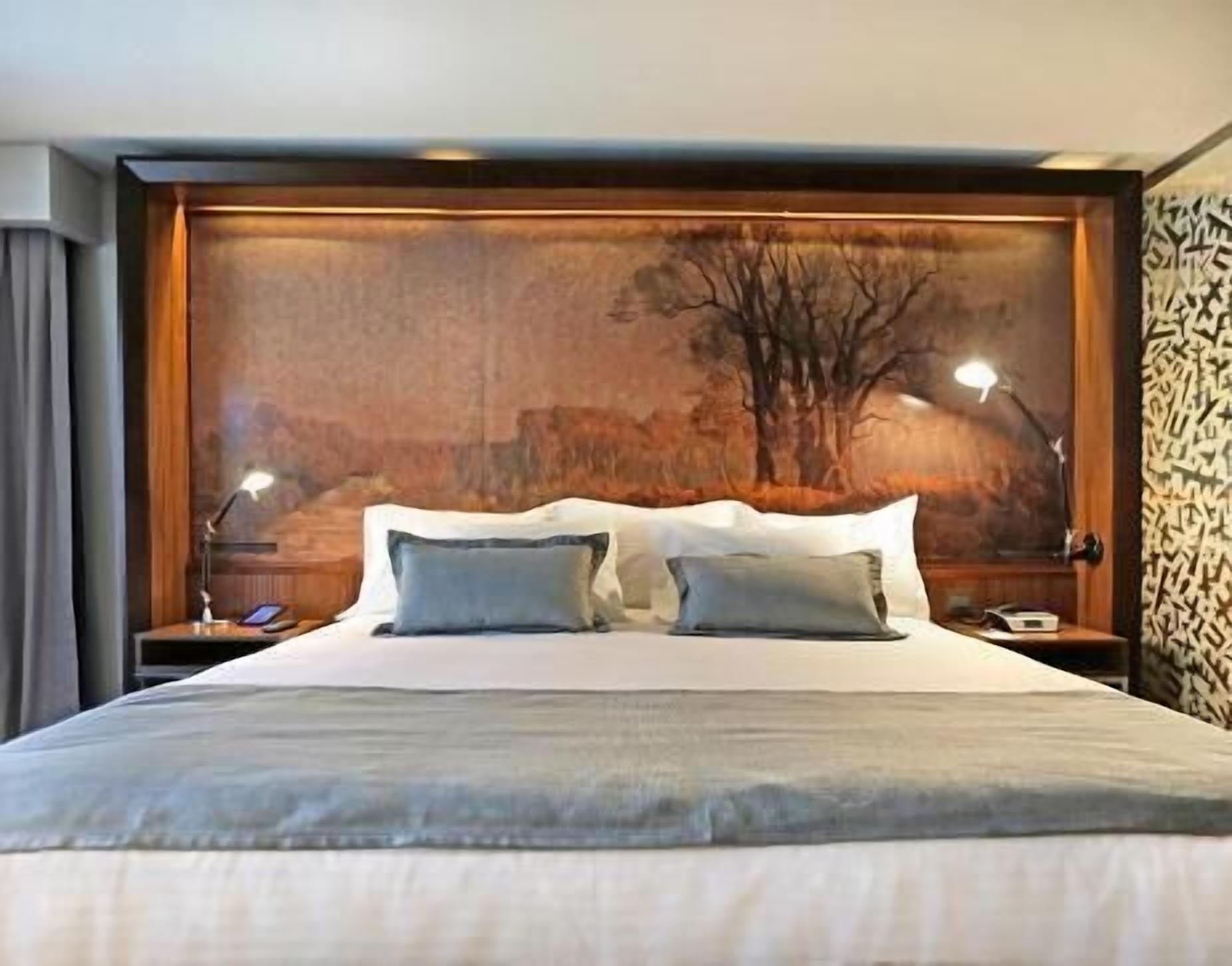 A large bed with two pillows, a wooden headboard, and a nightstand with a lamp.