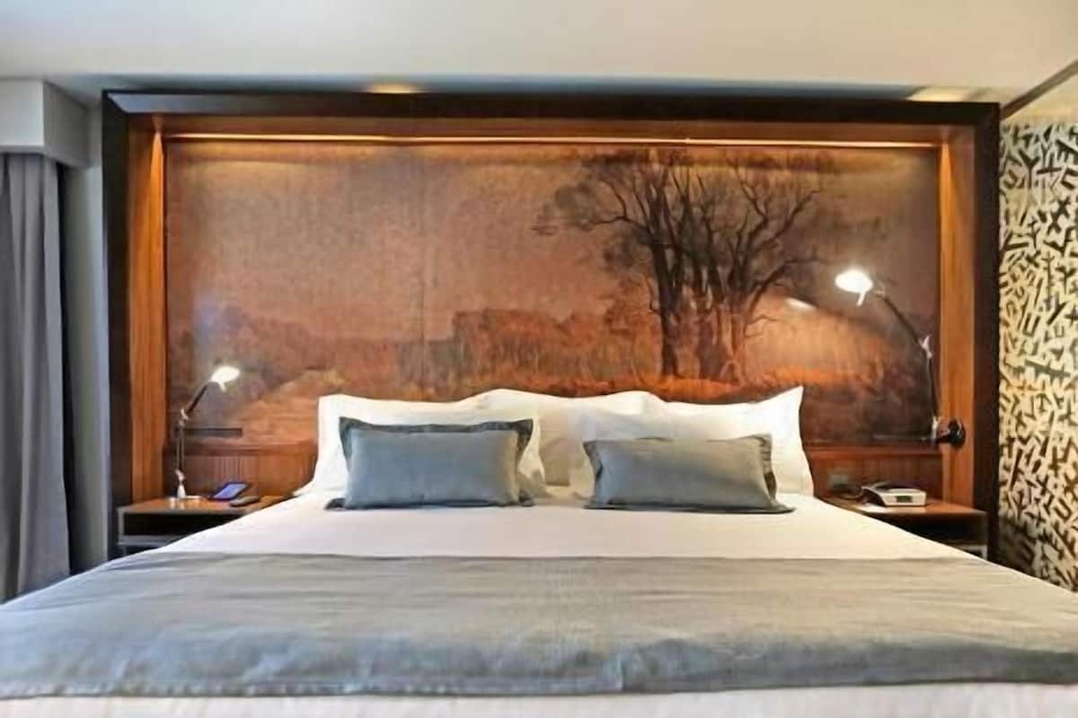 Una cama grande con dos almohadas, un cabecero de madera y una mesita de noche con una lámpara.