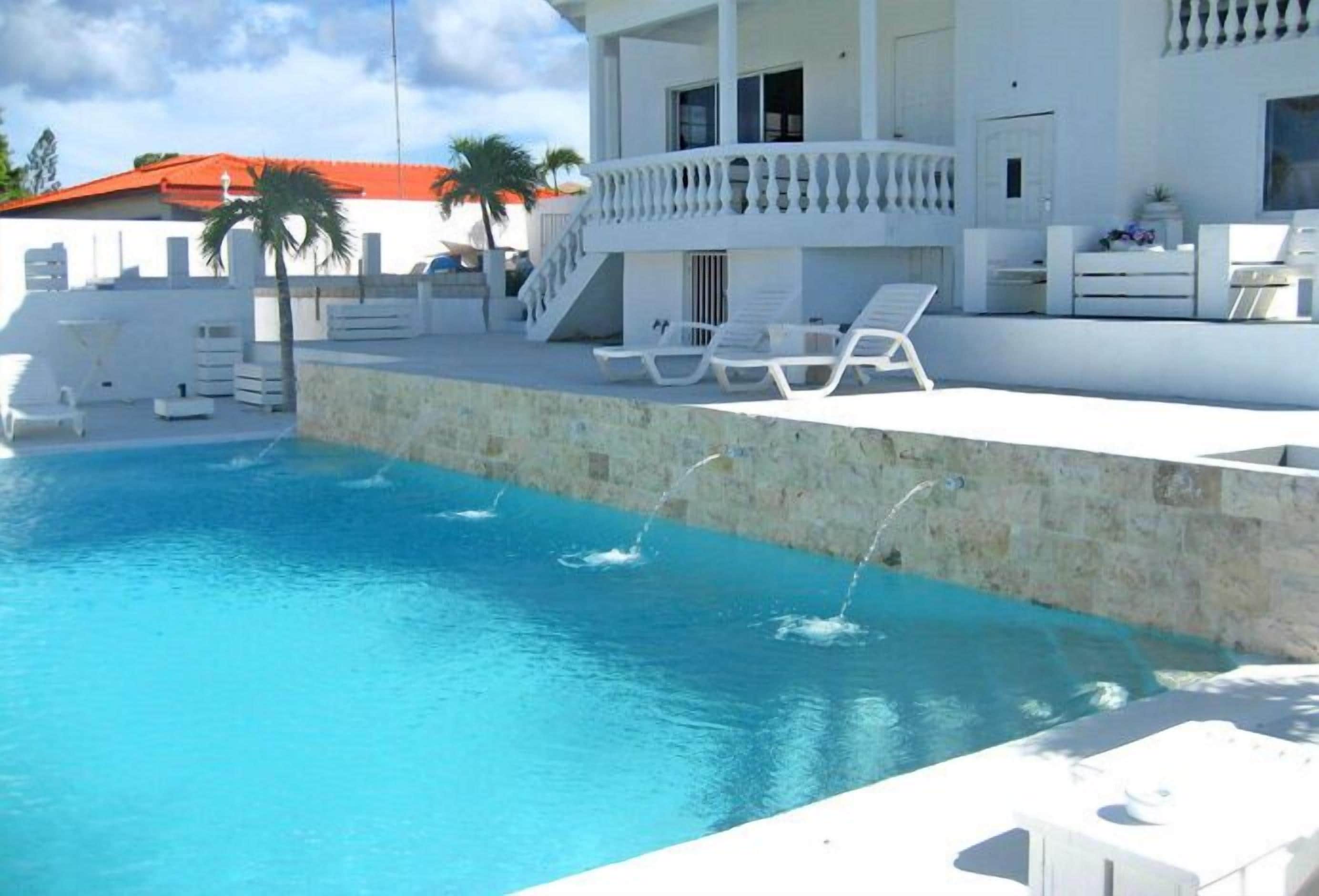 A pool area with a stone wall, lounge chairs, and a staircase leading to a balcony.