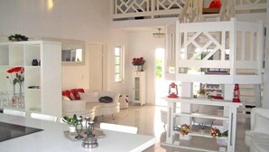 Un espacio de sala moderno con una decoración blanca, que incluye una mesa de comedor, sofás blancos y una escalera blanca.