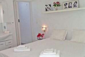 A hotel room with a bed, a bedside table with a lamp, a mirror, and a shelf with pictures and flowers. - Champartments Villa & Apartments Cristal (Jan Thiel)
