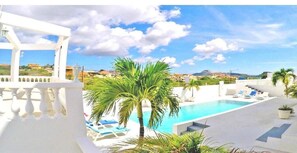 A pool area with a white structure, palm trees, and a view of distant buildings. - Champartments Villa & Apartments Cristal (Jan Thiel)