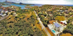An aerial view of a coastal town with a prominent white building with a blue roof, surrounded by greenery and a road leading to the sea. - Champartments Villa & Apartments Cristal (Jan Thiel)