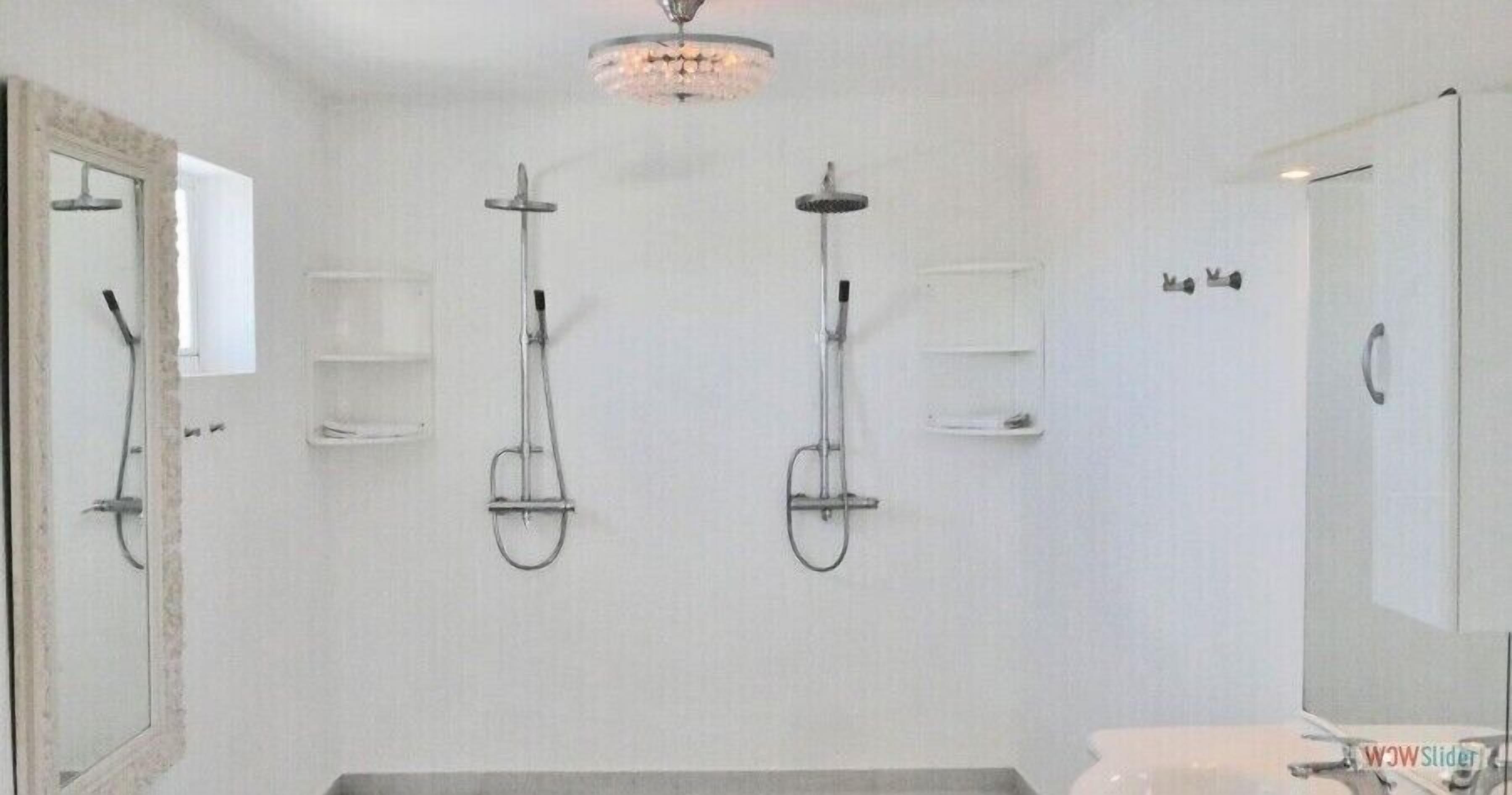 A bathroom with three wall-mounted showers, a toilet, and a large mirror.