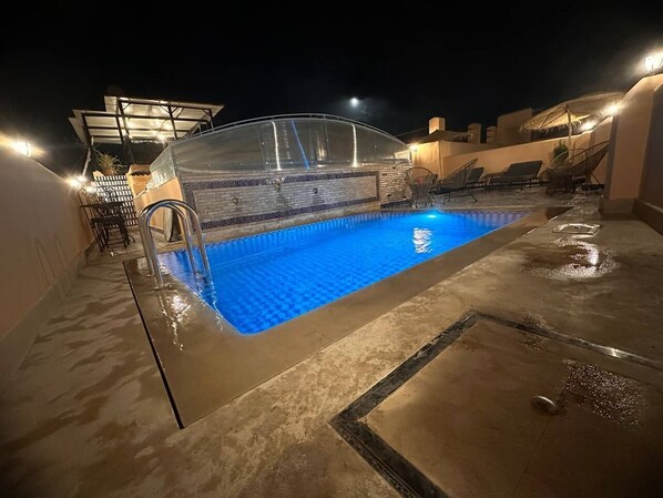 Una piscina en la azotea con cerramiento de vidrio, sillones de descanso y un área de estar cubierta.