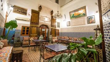 Un intérieur marocain traditionnel, avec des carreaux décoratifs, un lustre et différents types de sièges.