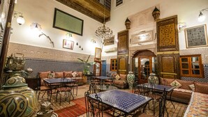 A traditional Moroccan interior with ornate tile work, a chandelier, and a variety of seating arrangements. - Riad Dar Tahri & SPA (Fes)