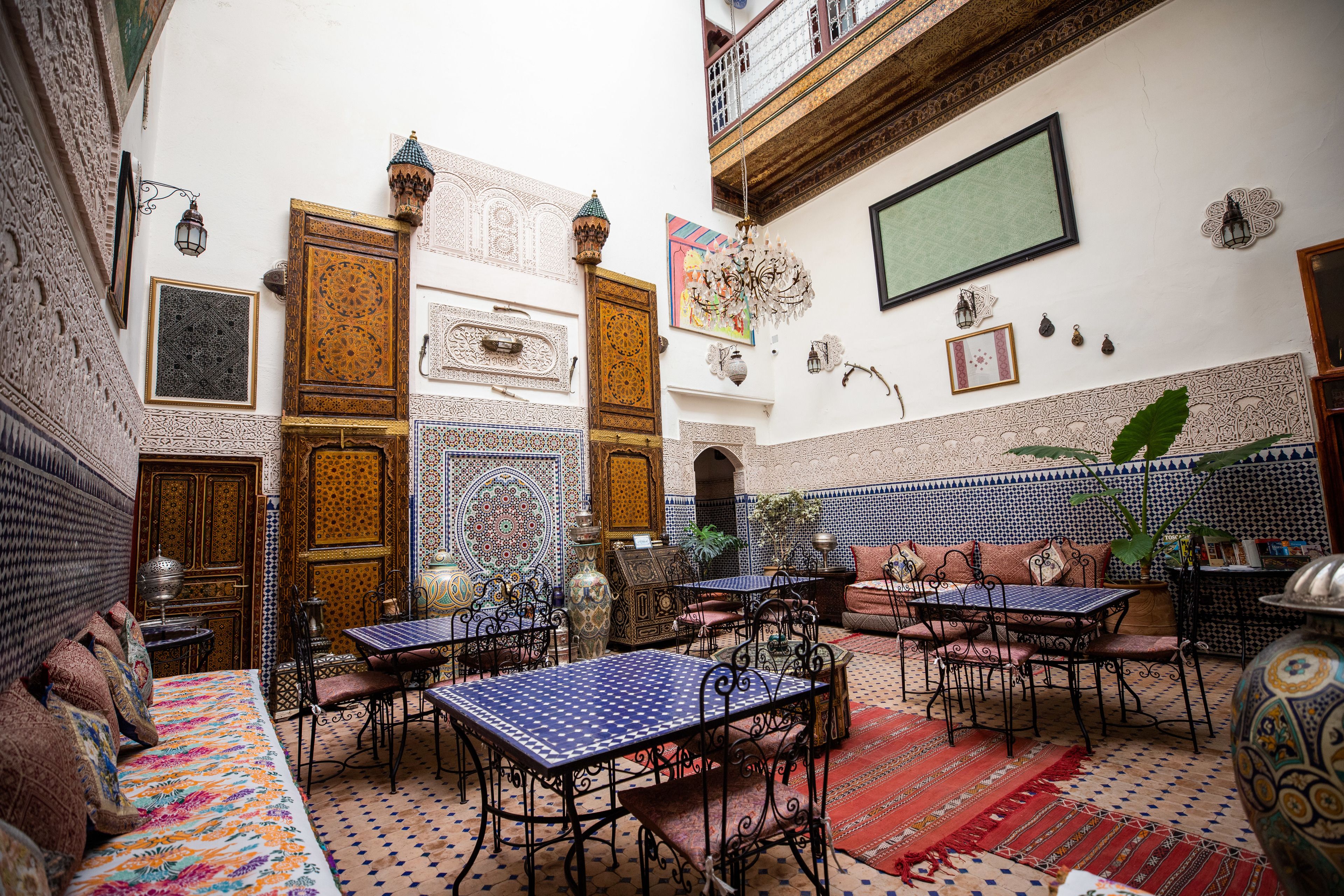 Um interior marroquino tradicional com portas ricamente decoradas, paredes com padrões e uma variedade de opções de assento, incluindo sofás e mesas.