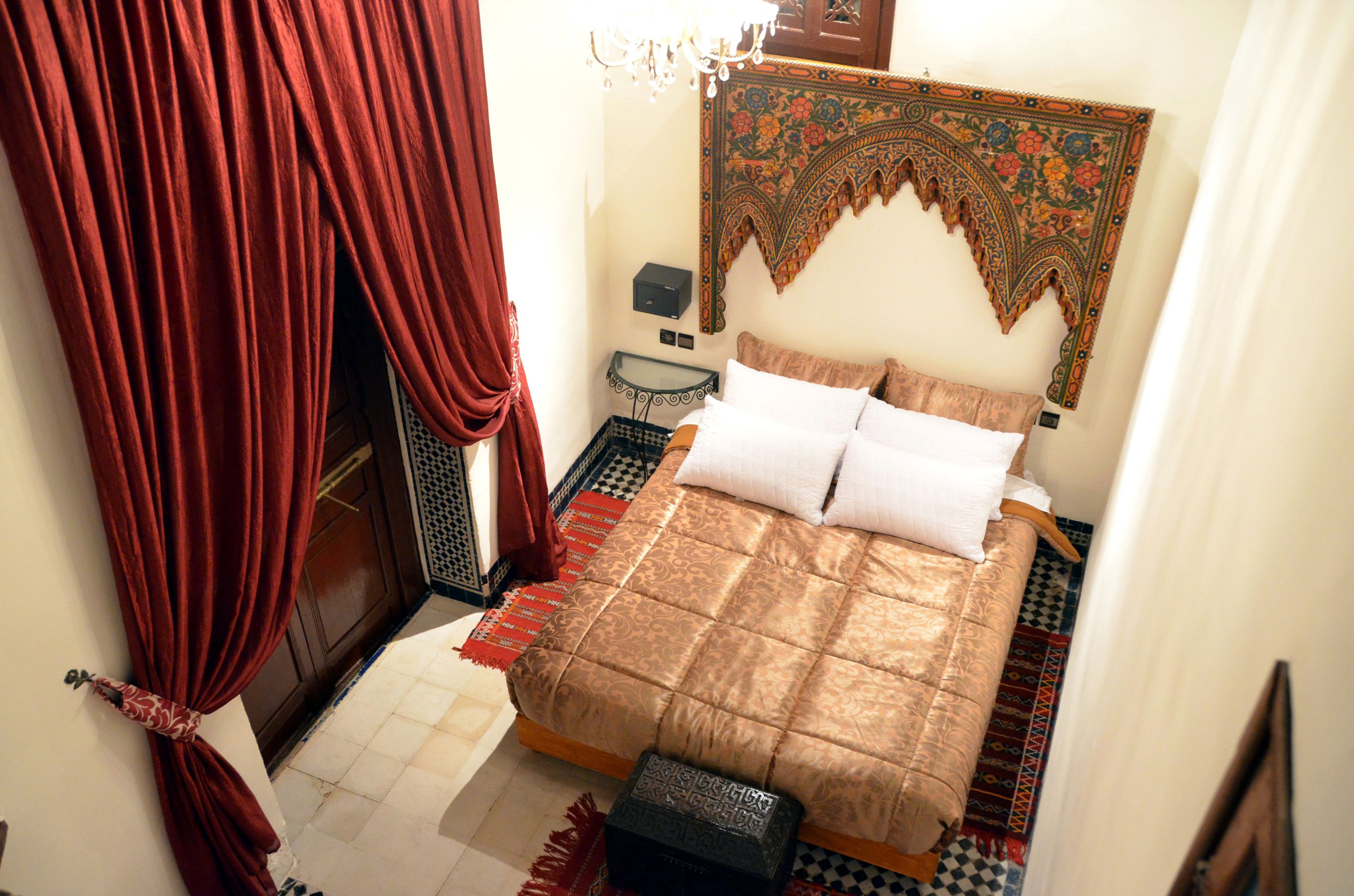 Un dormitorio con cama, mesita de noche, un tapiz de pared y una cortina roja.