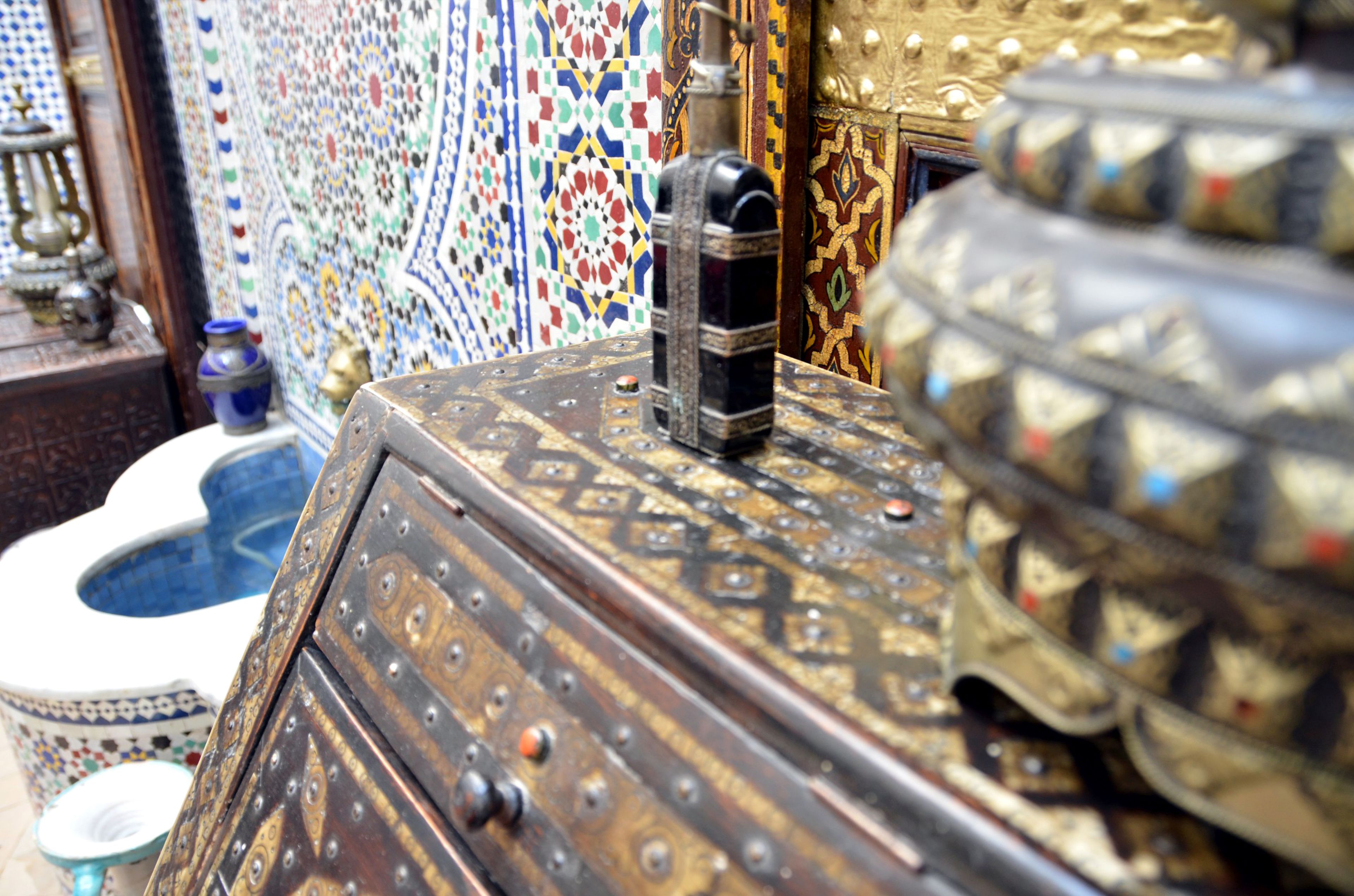 A traditional Moroccan room with a wooden chest, a brass door, and a tiled wall.