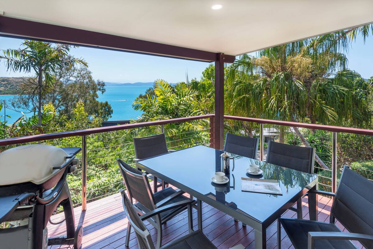 A balcony with a glass table, chairs, and a grill.