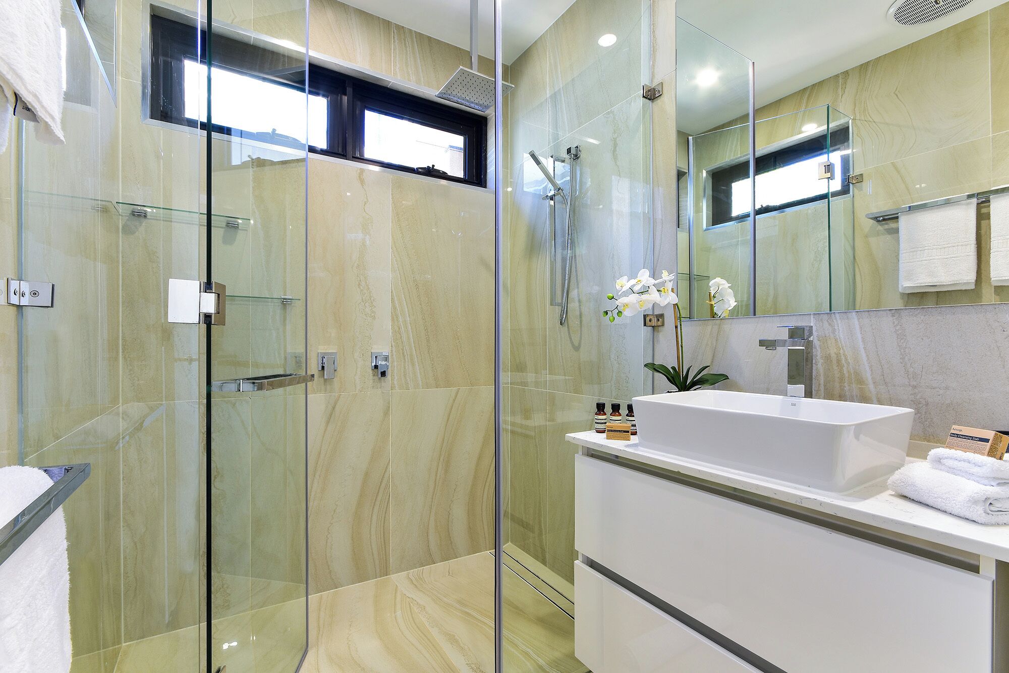 A modern bathroom with a glass-enclosed shower, a white sink, and a large mirror.