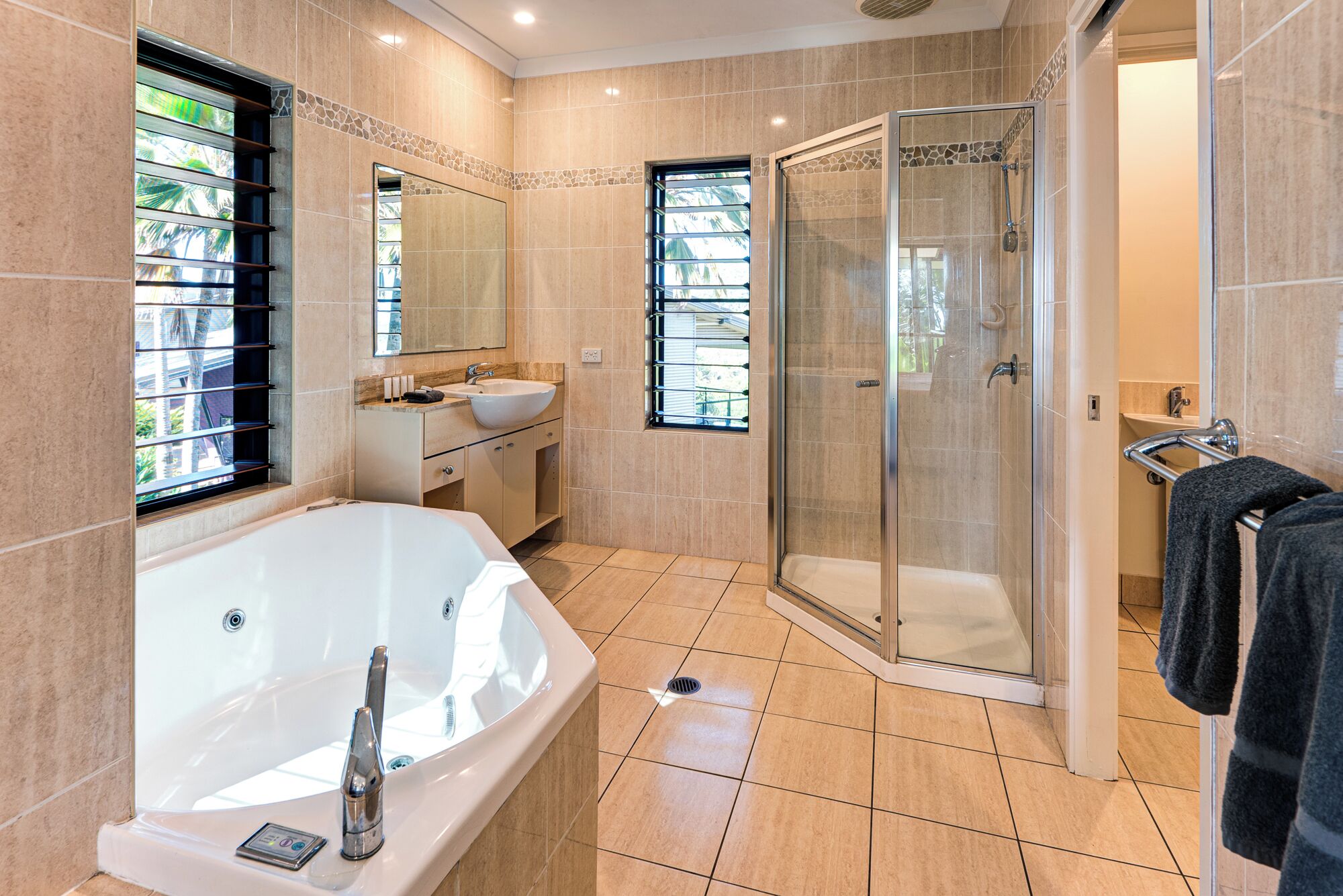 A modern bathroom with a bathtub, a glass-enclosed shower, a vanity with a sink, and a window with blinds.