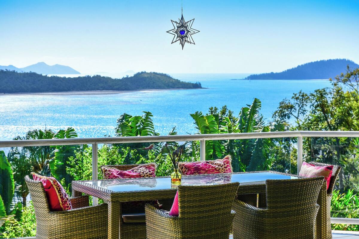 A balcony with wicker furniture, a glass table, and a hanging star decoration.