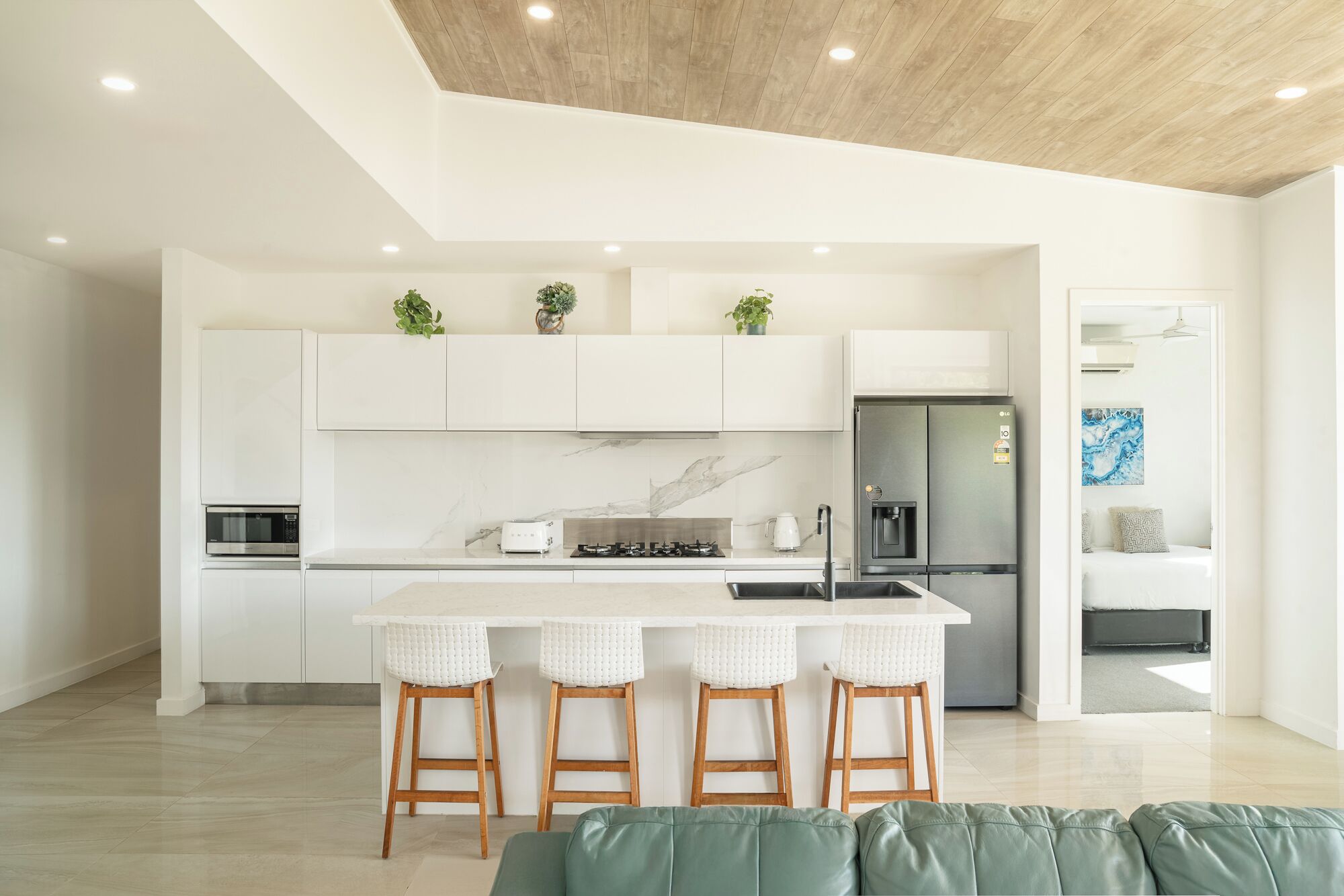 Une cuisine moderne avec des meubles blancs, un pare-feu en marbre, un réfrigérateur en acier inoxydable et un îlot central doté de tabourets de bar.