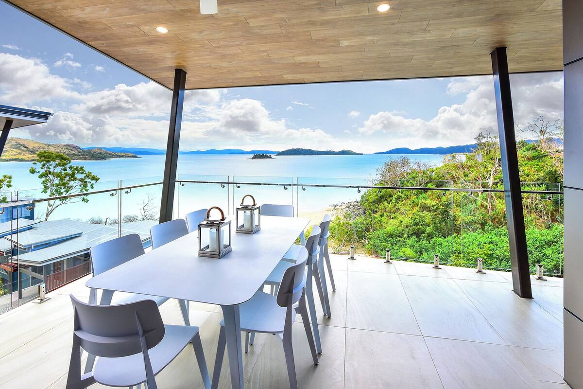 A dining area with a table and chairs, overlooking a scenic view of a lake and hills.